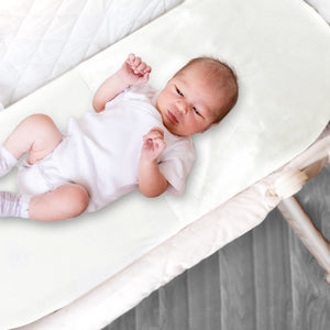 Baby laying in a Moses basket featuring a fitted satin sheet